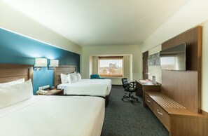 Une chambre d’hôtel avec deux lits, un bureau, une chaise, une télévision et une fenêtre donnant sur la ville.