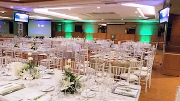 Un salón de banquetes con varias mesas redondas dispuestas para comer, equipado con manteles blancos, sillas y cristalería.