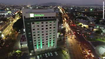 Un edificio de varios pisos con un llamativo letrero de 'Holiday Inn', rodeado de calles transitadas y luces de la ciudad.