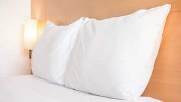 Una cama bien tendida con ropa blanca y una sola almohada blanca.