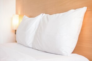 A neatly made bed with white bedding and a single white pillow against a wooden headboard. - Holiday Inn Guadalajara Expo by IHG (Zapopan)