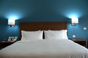 Una habitación de hotel con una cama grande, dos mesitas de noche, una lámpara de pared y un teléfono.