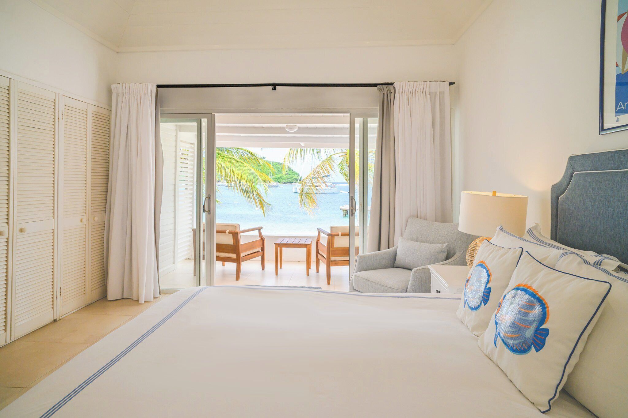 Une chambre d’hôtel avec un lit, un bureau, deux chaises, une vue sur la mer et un balcon avec des rideaux.