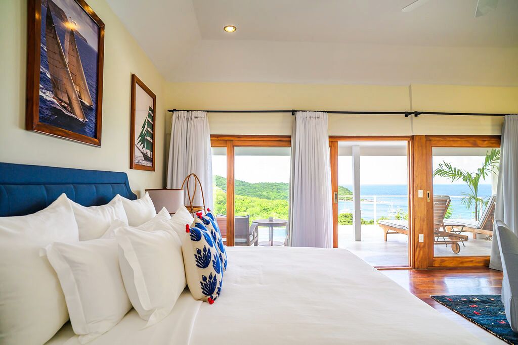 A bedroom with a large bed, a view of the ocean, and a balcony with outdoor seating.