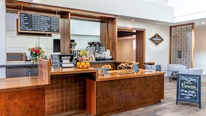 Een toonbank van een koffiebar met een menubord, een koffieapparaat en een bordje met de tekst 'Wow Open Coffee Corner'.