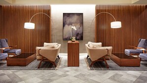 Een moderne lobby met twee banken, een kleine houten tafel en een groot abstract schilderij aan de muur.
