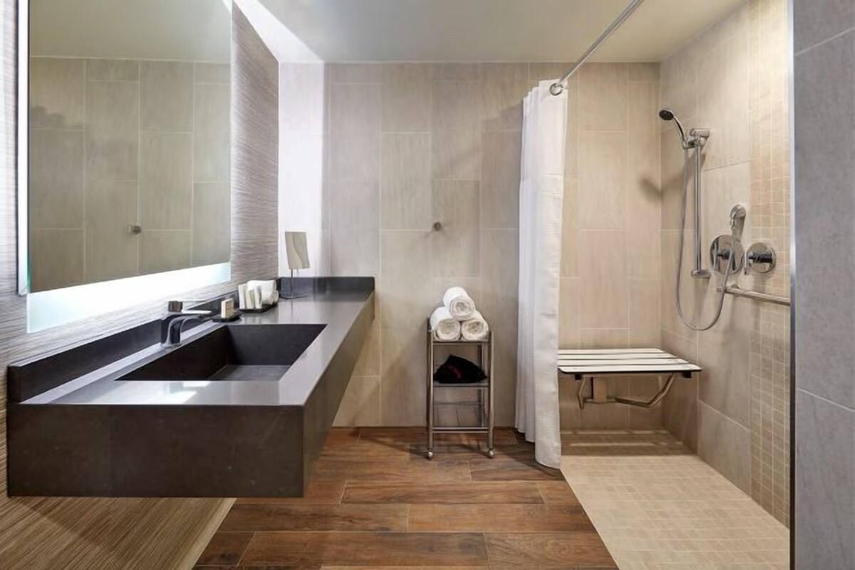Une salle de bain moderne avec un grand lavabo foncé, une douche équipée d’un pommeau de douche à main et un porte-serviettes avec des serviettes.