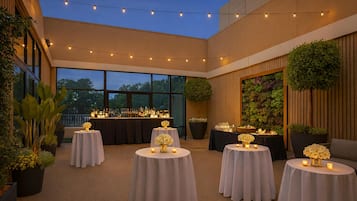 An outdoor patio area with round tables, string lights, and potted plants.