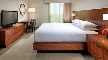 A hotel room with a large bed, a television, a desk with a chair, and a window with curtains.