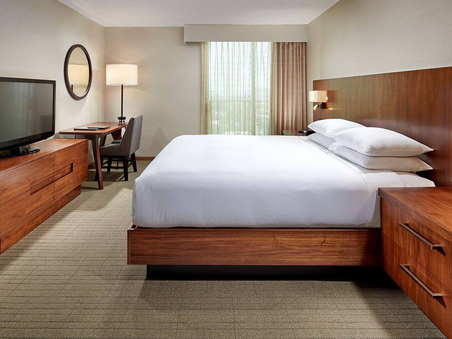 A hotel room with a large bed, a television, a desk with a chair, and a window with curtains.