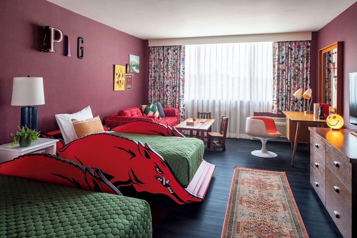 A hotel room with a bed, a desk, a chair, a lamp, and a rug.