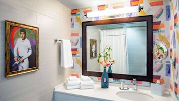 A bathroom with a large mirror, a framed portrait, a sink with a vase of flowers, and towels.