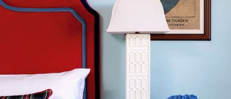 A neatly made bed with a red headboard, a white lamp, and a framed picture on the wall.