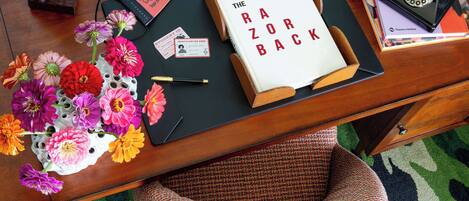 A desk with a book titled "The Razorback," a telephone, a figurine, a card, and a vase with flowers.