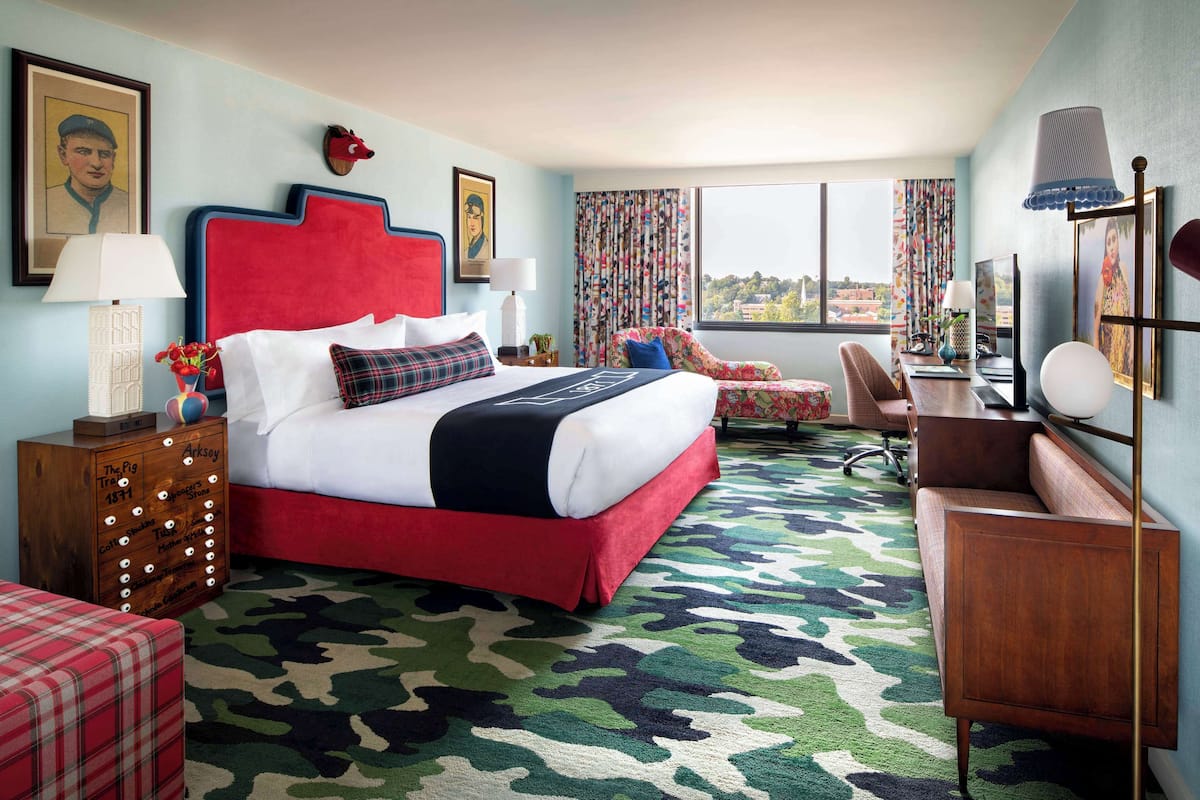 A hotel room with a large bed, a desk, a chair, and a view of the city.