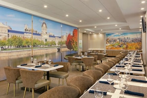 A restaurant with long tables, chairs, and a mural of a cityscape and river.