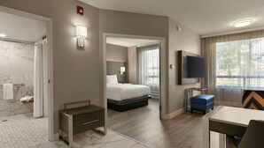 Une chambre d’hôtel comprenant un lit, un bureau, une télévision, un banc et une salle de bain avec douche et toilettes.