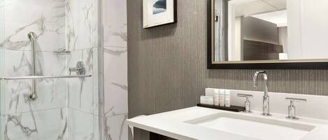 A modern bathroom with a marble shower, a large sink with two faucets, and a framed picture on the wall.
