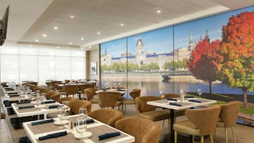 Een restaurant met meerdere tafels en stoelen, grote ramen en een muurschildering van een stadsgezicht.