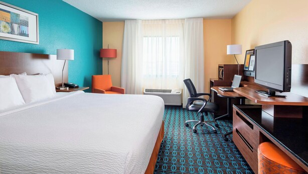 A hotel room with a large bed, a desk with a computer, a chair, and a television.