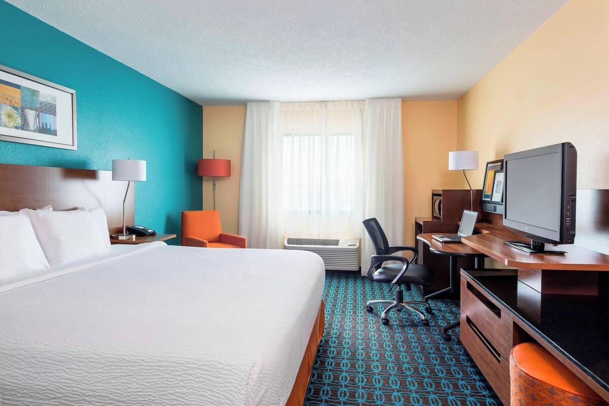 A hotel room with a large bed, a desk with a computer, a chair, and a television.