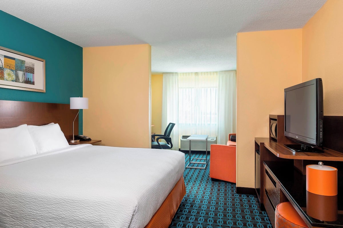 A hotel room with a large bed, a desk with a television, a chair, and a window with curtains.