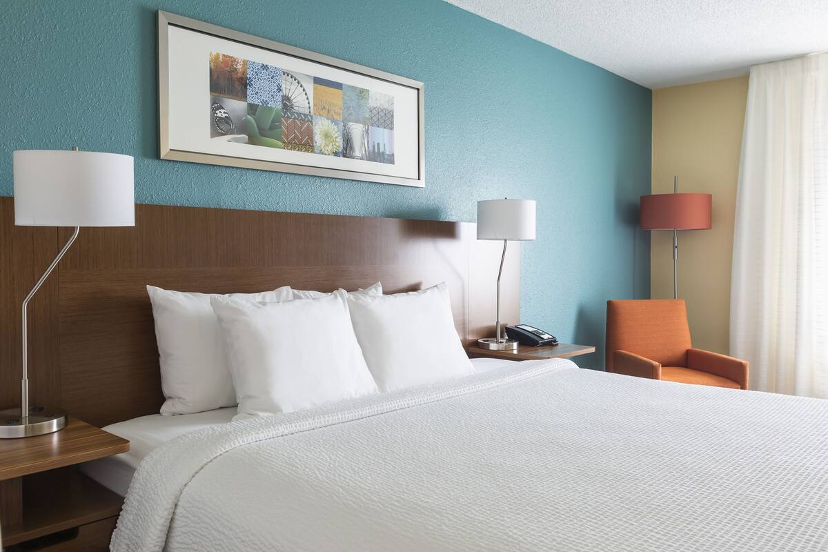 A hotel room with a large bed, two bedside tables, a chair, and a painting on the wall.