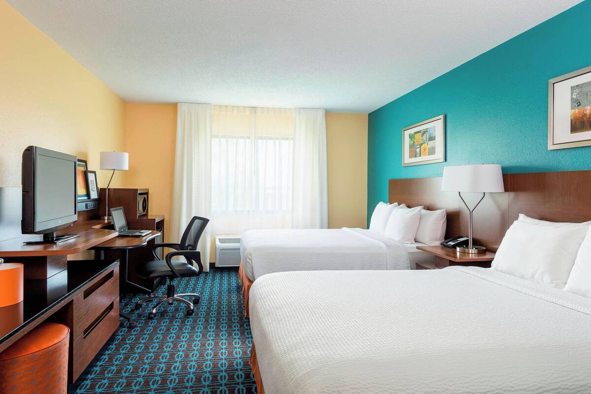 A hotel room with two beds, a desk with a computer, a television, and a lamp.