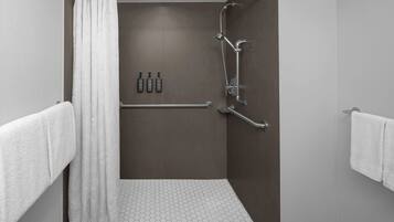 A shower area with a white shower curtain, a handrail, and a tiled floor.