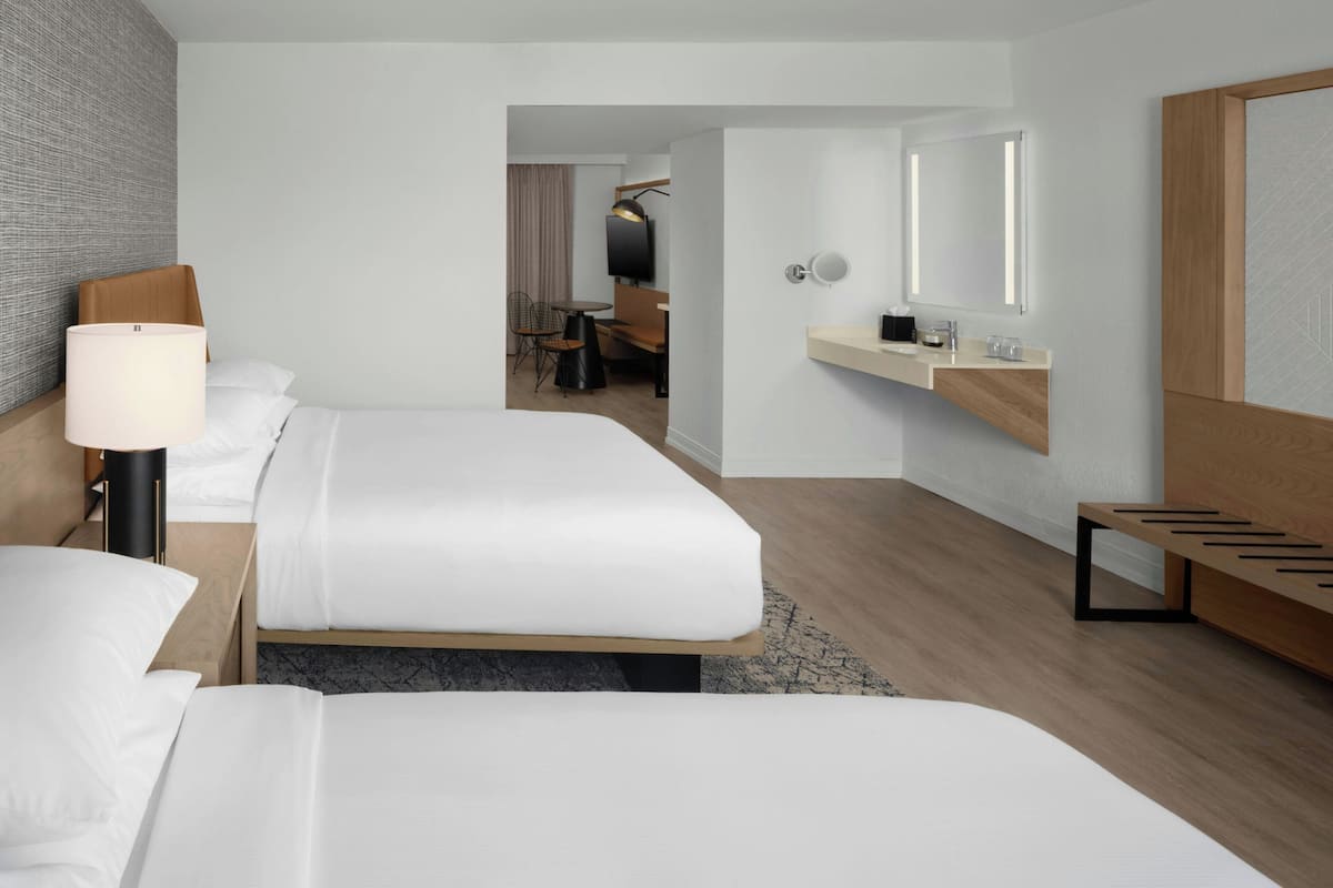 Ein Hotelzimmer mit zwei Betten, einem Schreibtisch, einem Stuhl, einem kleinen Tisch, einem Spiegel und einer Holzbank.