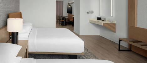 A hotel room with two beds, a desk, a chair, a small table, a mirror, and a wooden bench.