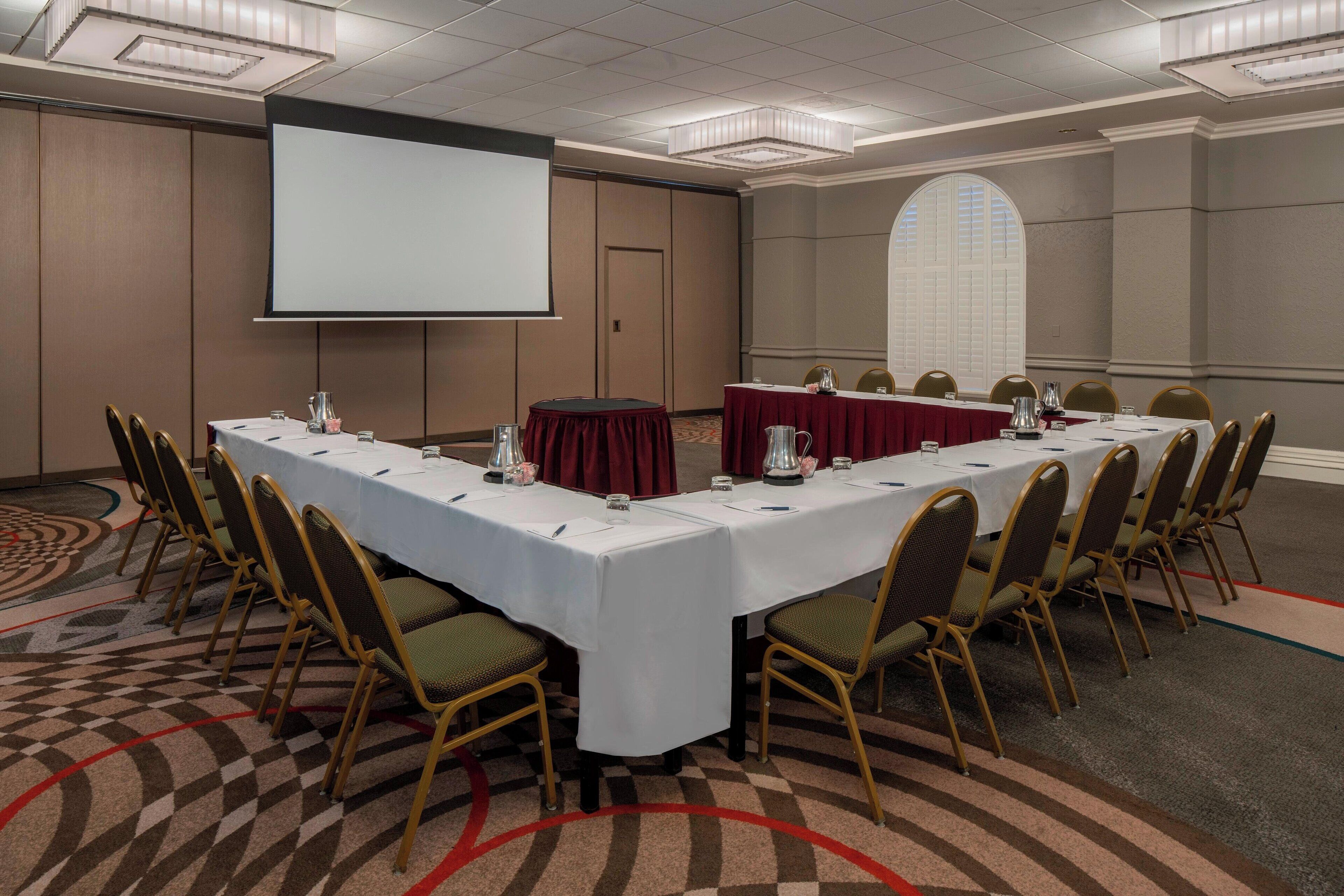 A conference room with a long table, chairs, a projector screen, and a large window.