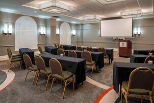 Un salón de conferencias con mesas, sillas, una pantalla de proyector y un atril.