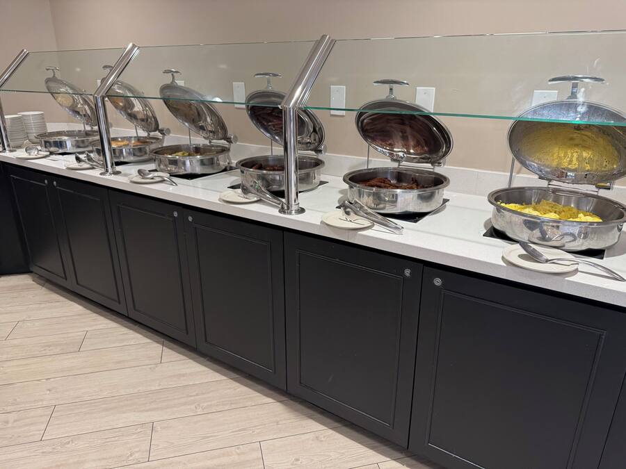 Een buffet met diverse gerechten, waaronder een schaal gele rijst, een bak bruine saus en een schaal gemengde groenten.
