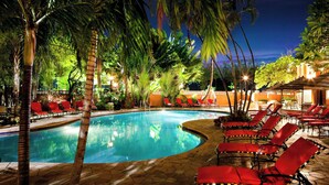 A swimming pool surrounded by palm trees and red lounge chairs.