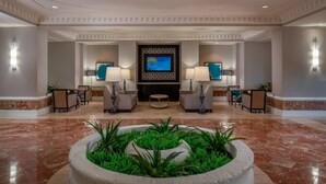A lobby with a reception desk, two armchairs, a coffee table, and a television screen.