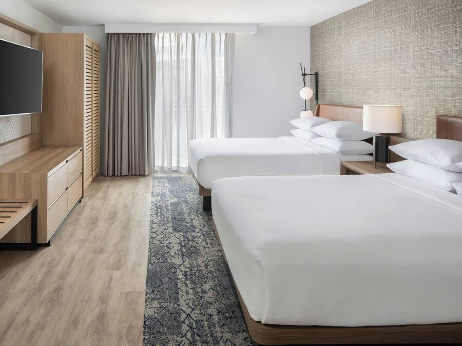 Een hotelkamer met twee bedden, een televisie, een bureau en een groot raam met gordijnen.