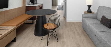 Una habitación moderna con una mesa redonda, una silla de estructura metálica, un sofá, un televisor y una lámpara.
