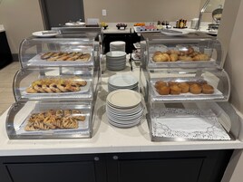 Buffet com diversos produtos de panificação expostos em embalagens de plástico transparente.