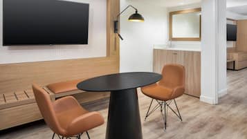 A modern room with a round black table, two brown chairs, a mounted TV, and a wall-mounted lamp.