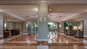 A spacious lobby with marble flooring, a reception desk, and a column with the logo 'spg'.