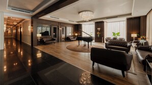 Un vaste espace de vie agrémenté d’un magnifique piano à queue, de canapés en cuir et d’un lustre.