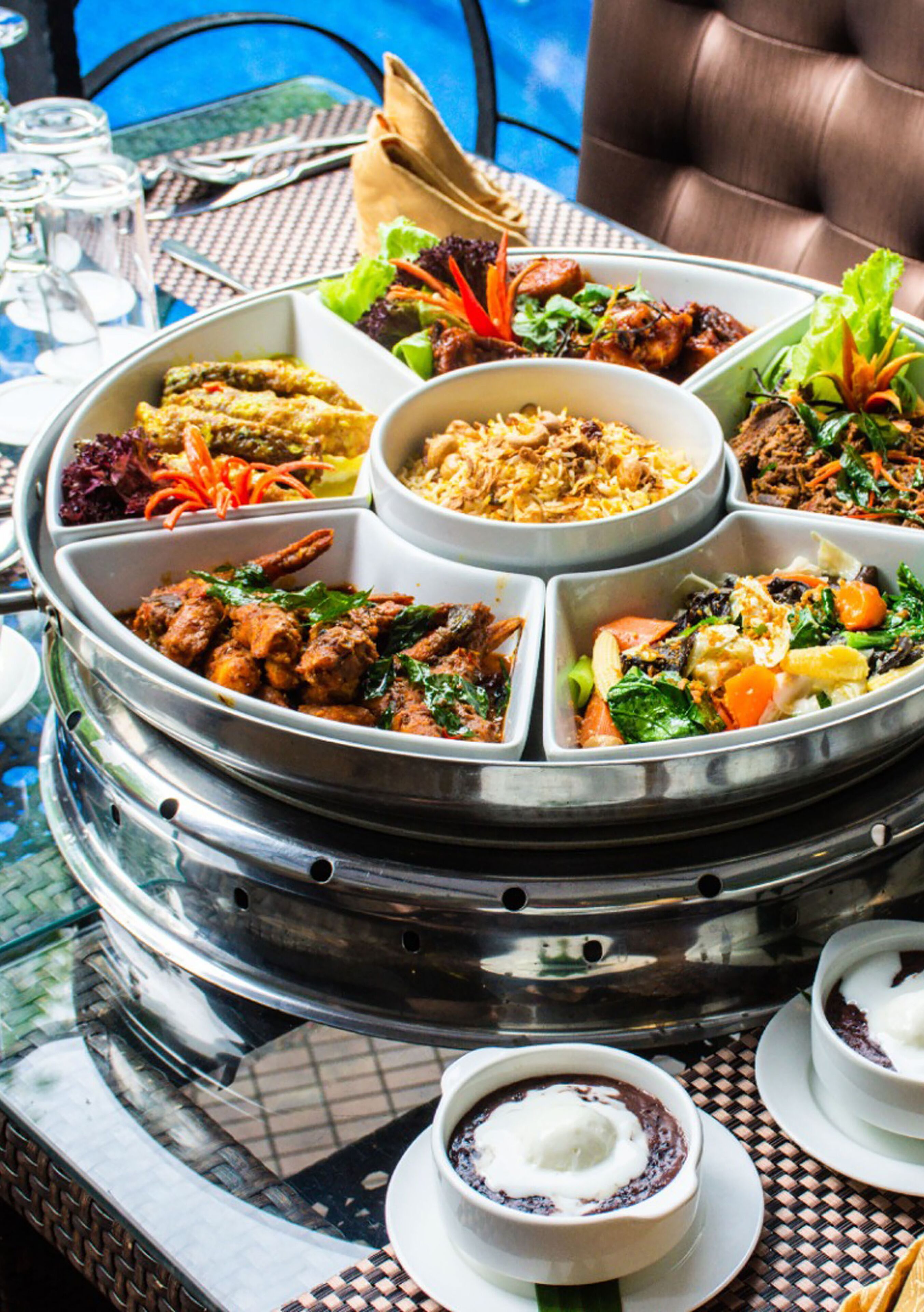 A buffet with various dishes arranged in a central serving tray, surrounded by a dining table with chairs.