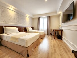 Habitación de hotel con dos camas, un escritorio, una silla, un televisor y un ventanal con cortinas.