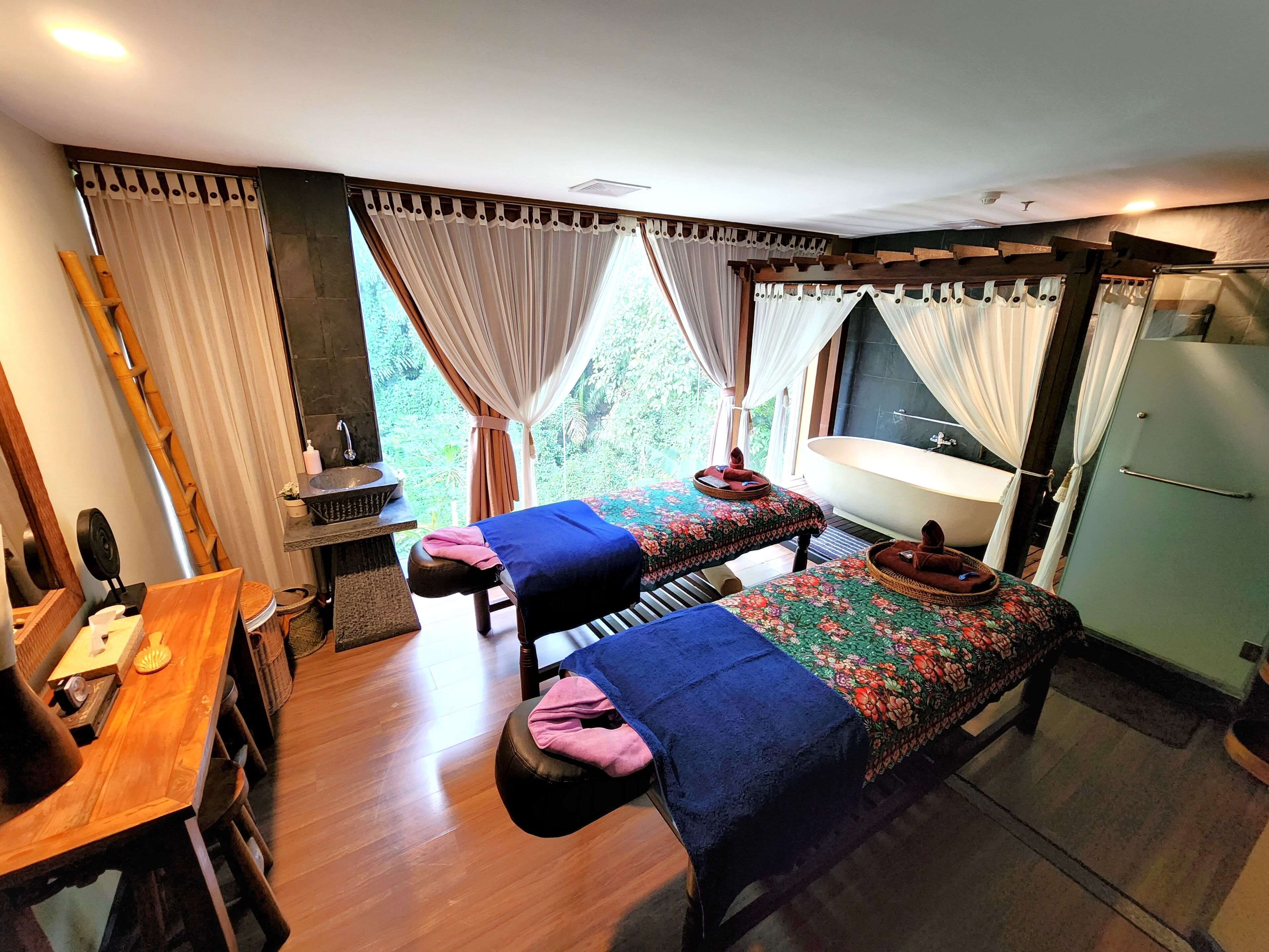 A room with two beds, a wooden table, a sink, and a bathtub.