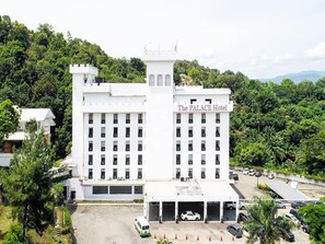 Un hôtel à plusieurs étages doté d’une tour centrale, appelé « The PALACE Hotel », qui offre un grand parking et un décor luxuriant en arrière-plan.