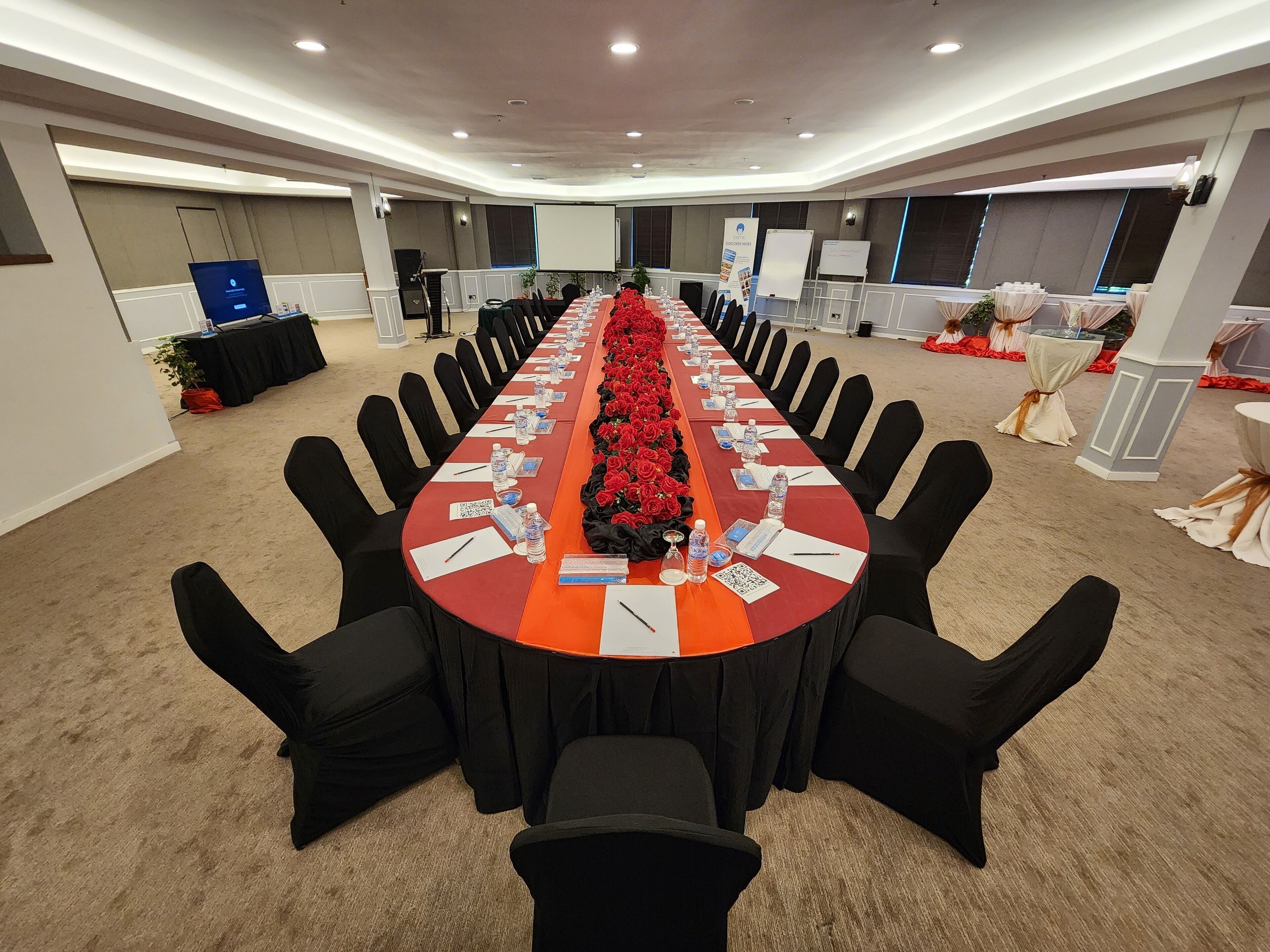 A conference room with a long table, black chairs, and red floral arrangements.