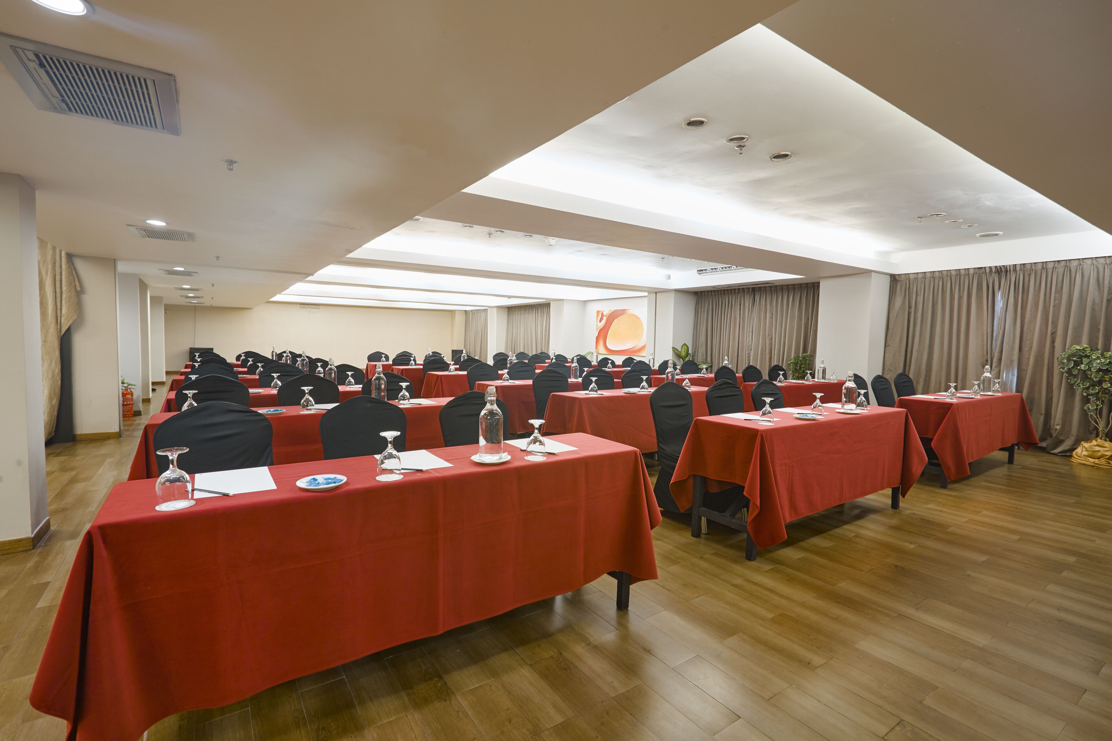 A conference room with multiple tables, each covered with a red tablecloth, equipped with chairs, water glasses, and notepads.