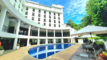 Un hotel moderno con piscina central, mobiliario exterior y un patio con un edificio blanco.