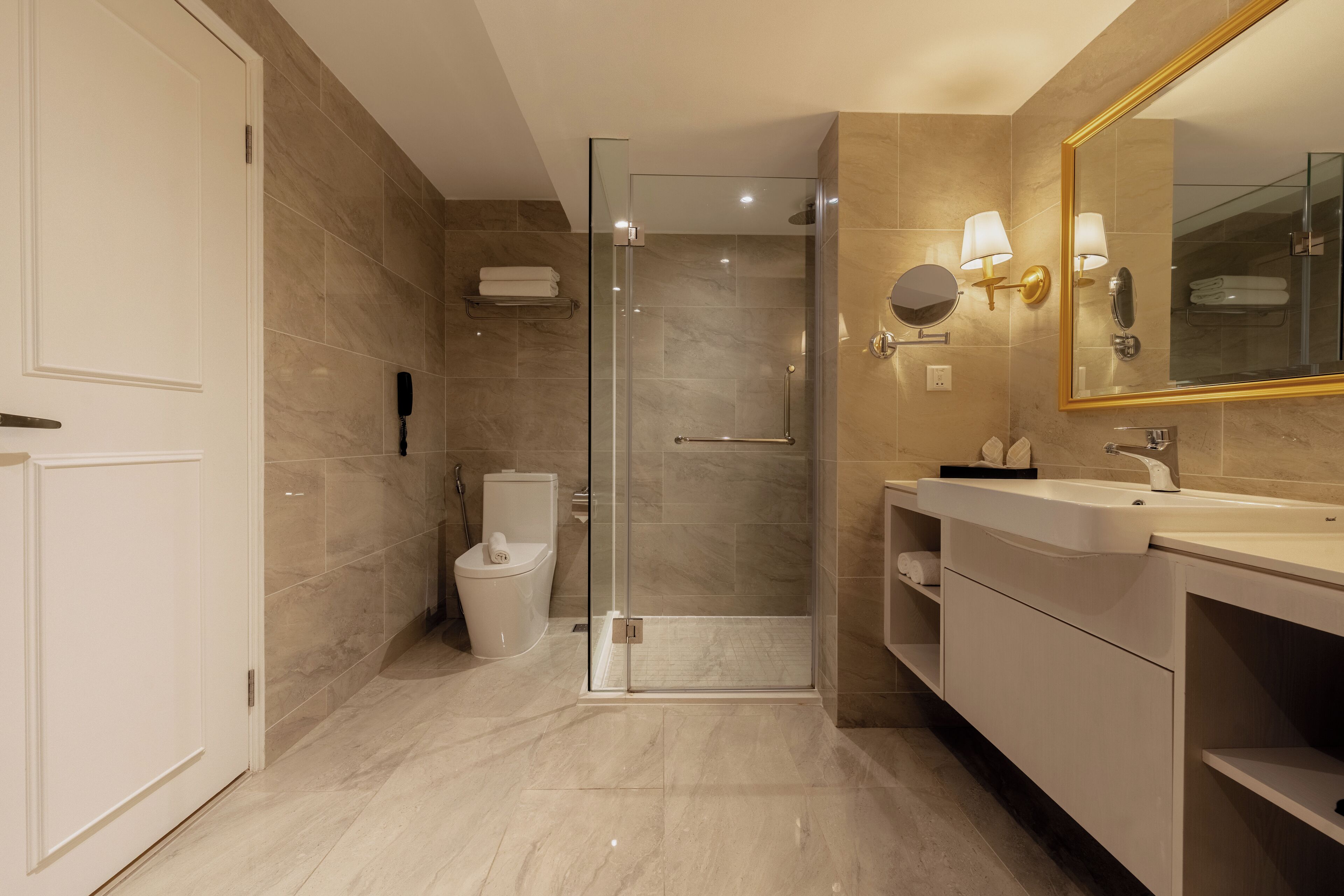 A modern bathroom with a glass-enclosed shower, a white toilet, and a vanity with a mirror and lights.